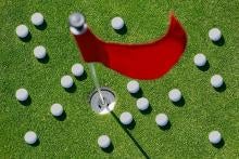 Golf balls scatterd on the green around a golf hole and flag.